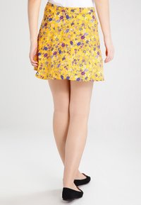 Gonna gialla con un motivo floreale in viola, rosa e bianco. Forma ad A, lunghezza sopra il ginocchio, realizzata in tessuto leggero.