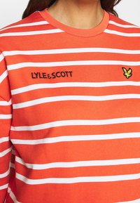 Sudadera de algodón a rayas naranjas y blancas con el logo bordado de "LYLE & SCOTT" y un emblema de águila amarilla en el pecho.