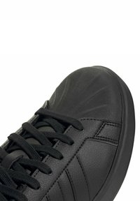 Chaussure de sport noire avec une tige en cuir lisse, un bout renforcé texturé et des lacets ronds. Présente des rayures latérales discrètes et une semelle rembourrée.