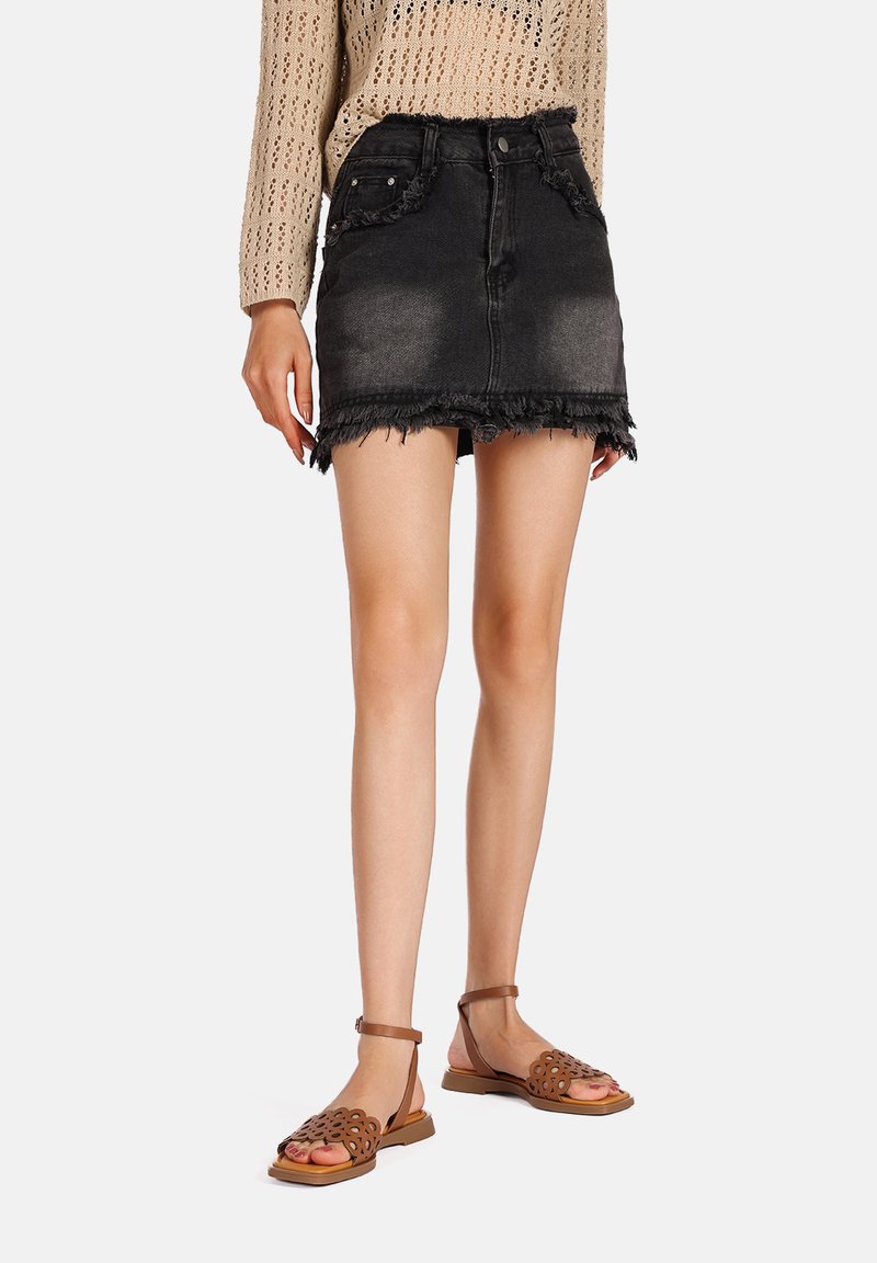 Gonna di jeans nera con orlo sfrangiato, due tasche frontali e una forma aderente, abbinata a sandali marroni decorati con fiori.