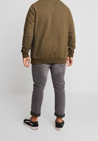 Felpa a maglia verde oliva con motivo a trama, polsini e orlo a coste, abbinata a jeans grigi arrotolati e sneakers nere.