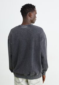 Donkergrijze sweatshirt met een ontspannen pasvorm, ribbelboord aan de ronde hals en omgeslagen mouwen. De stof vertoont een vervaagde textuur met zichtbare stikselaccenten.