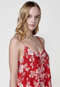 Camisole rouge à motifs floraux avec de fines bretelles. Présente des motifs floraux blancs et une coupe fluide. Tissu léger et doux avec une coupe décontractée.