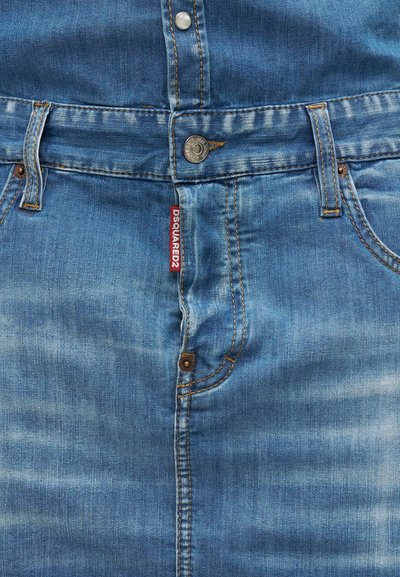 Μπλε τζιν από denim σε κοντινό πλάνο που δείχνει κλείσιμο με κουμπί, θηλιές για ζώνη, μπροστινές τσέπες και μια κόκκινη υφασμάτινη ετικέτα με την ένδειξη "DSQUARED2."