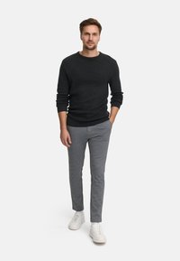 Szary sweter o fakturze, jasnoszare spodnie slim-fit i białe sneakersy. Mężczyzna stoi pewnie, ręce w kieszeniach, na neutralnym tle.