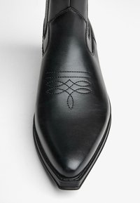 Črne usnjene oblečne čevlje s koničastim nosom. Imajo dekorativno šivanje in vdelan vzorec blizu nosu. Eleganten, gladek izgled.