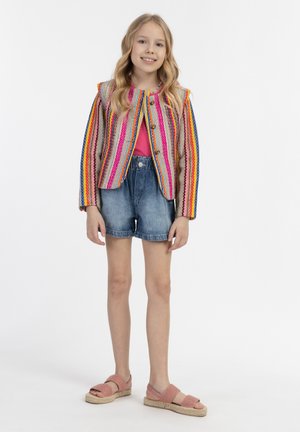 Gestreifte Strickjacke in Pink, Blau und Gelb über einem pinken Oberteil, kombiniert mit Jeansshorts und hellrosa Espadrilles.