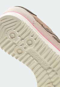 Potplat tenisice od svijetloružičaste antilop kože s bijelim gumiranim gaznim slojem; sadrži kružne naglaske i brendirani natpis "adidas" sa strane. Uzorak površine za prianjanje s teksturom.