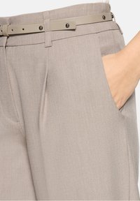 Pantalon beige clair avec une texture subtile, présentant une coupe ajustée, des poches latérales, et une ceinture assortie avec une boucle détaillée.