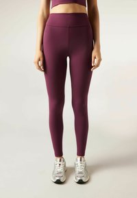 Bordové legíny vyrobené z elastického materiálu s vysokým pasem, hladkým povrchem a plnou délkou, zkombinované se stříbrnými sportovními botami.
