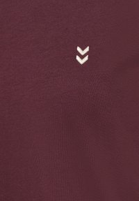 Burgunder T-shirt lavet af glat stof med et broderet hvidt chevron-design på brystet, i en tætsiddende form og blød tekstur.