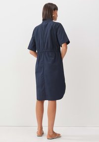 Navy-blaues Shirtkleid mit kurzen Ärmeln, tailliert und mit Taschen. Glattes Material mit einer lässigen Passform, knielanges Design.
