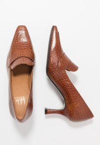 Zapatos de tacón altos de color marrón con estampado de cocodrilo, con punta afilada, una correa en la parte delantera y un tacón delgado, que presentan un acabado suave y brillante.