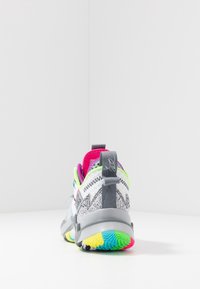 Buty sportowe z wielokolorową podeszwą w zygzakowy wzór, szaro-białą cholewką oraz różowymi i zielonymi akcentami na kołnierzu i wnętrzu.