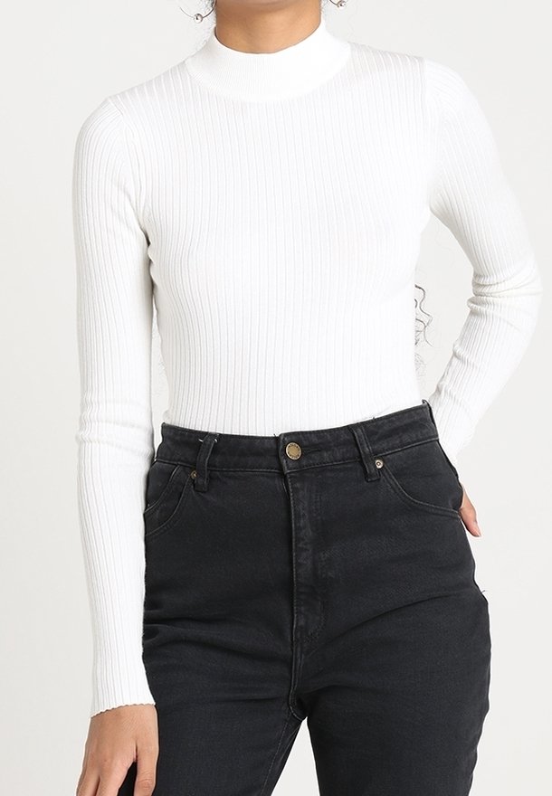 Weißes geripptes Rollkragenoberteil mit langen Ärmeln, kombiniert mit schwarzen High-Waist-Jeans mit vorderen Taschen und goldfarbenen Details.