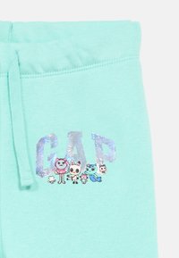 Παντελόνι φόρμας σε χρώμα μέντας με λαμπερό λογότυπο "GAP" και σχέδια με καρτουνίστικα ζώα. Το υλικό είναι μαλακό, με ελαστική μέση και κορδόνι.