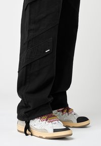 Zwarte cargo broek met zijzakken, gecombineerd met grijze en beige sneakers met kleurrijke veters en rubberen zolen.