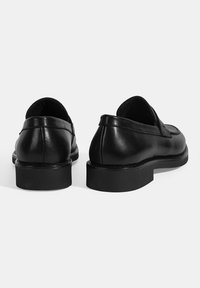 Schwarze Lederloafer mit glatter Textur, niedrigem Blockabsatz und schlichtem Design, das Stichdetails an der Rückseite und an den Seiten aufweist.