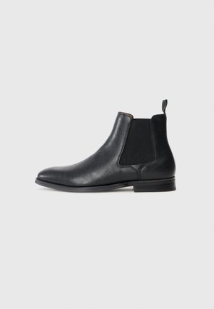 Botas Chelsea de cuero negro con paneles elásticos en los lados, textura suave, puntera redondeada y tacón bajo. Tirador verde en la parte trasera.