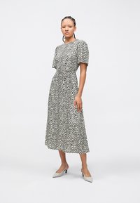 Φόρεμα σε ασπρόμαυρο πουά με σφηκο-σφιγμένη μέση, κοντά φουσκωτά μανίκια και μήκος μέχρι τη μέση της γάμπας. Συνδυάζεται με ανοιχτόχρωμα τακούνια.