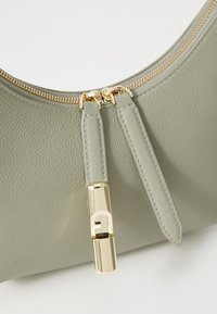 Borsa in pelle verde oliva con superficie texture, zip dorata e un dettaglio in metallo dorato con un design di lettere stilizzate.