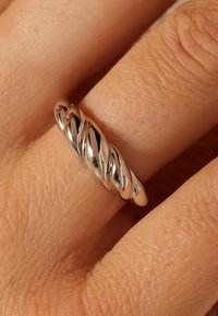 Sterling zilveren ring met een gedraaid ontwerp, met een gladde, gepolijste oppervlakte en subtiele reflecterende kwaliteit, gedragen aan een vinger.