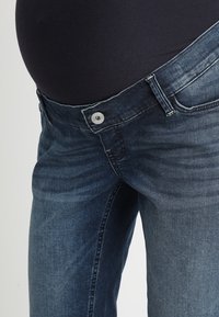 Graviditetsjeans i mörkblå denim med en mjuk yta, utrustad med knappstängning och ett stretchmidjeband för komfort.