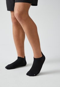 Schwarze Knöchelsocken aus einem weichen, dehnbaren Material mit gerippter Textur, im tiefen Schnitt und mit minimaler Markenkennzeichnung an der Seite.