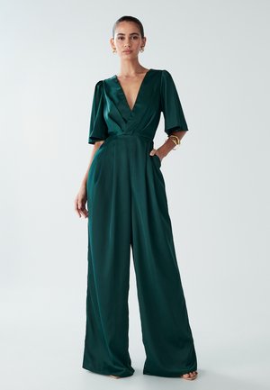 Combinaison vert émeraude en satin avec un décolleté en V profond, des manches courtes et larges, et un pantalon à jambes larges. Dotée de poches latérales et d'une taille cintrée.