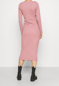 Långärmad, rosa bomull midi-klänning med en figursydd silhuett, featuring en rund halsringning och en jämn textur. Svarta ankelstövlar fulländar looken.