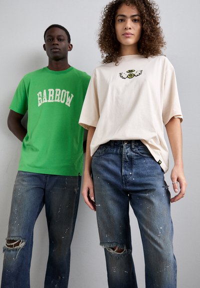 T-shirt en coton vert avec impression "BARROW", associé à un jean déchiré bleu clair avec des éclaboussures de peinture blanche. T-shirt beige avec un design brodé.