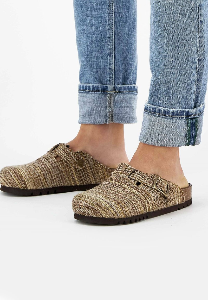 Sabots tissés, marron et jaune, à bout rond, avec une boucle en métal réglable et une surface texturée ; associés à un jean en denim retroussé.