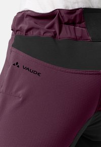 Pantalon d'extérieur bordeaux et noir avec une ceinture élastique et le logo "VAUDE" sur la cuisse supérieure.