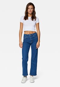 White cropped t-shirt, blue straight-leg jeans, and white sneakers. Denim has visible stitching; tee fits snugly at the waist.