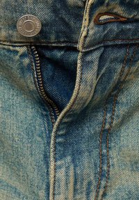 Jeans in denim azzurro chiaro con chiusura a zip e bottone, con cuciture marroni a contrasto e una texture sbiadita.