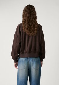 Brązowy zamszowy krótki sweatshirt z prążkowanym dołem, szerokimi rękawami i luźnym krojem, zestawiony z jasnoniebieskimi spodniami typu wide-leg z tylnymi kieszeniami.