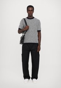 Grijs gespikkelde gebreide shirt met korte mouwen en marineblauwe boordjes, zwarte cargobroek en witte sneakers, geaccessorieerd met een zwarte schoudertas.