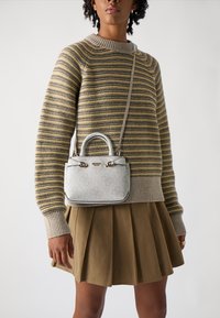 Miniature handbag in white leather with embossed pattern, dual handles, and silver hardware. Worn with a striped sweater and pleated skirt.