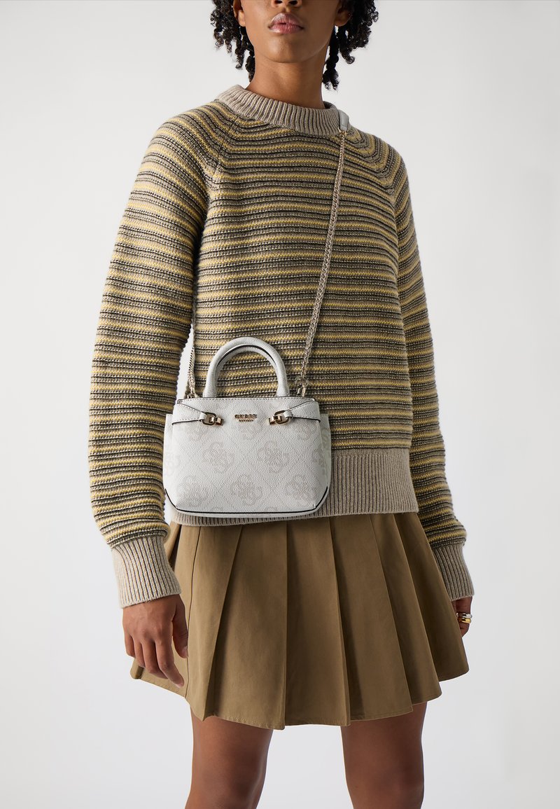 Miniature handbag in white leather with embossed pattern, dual handles, and silver hardware. Worn with a striped sweater and pleated skirt.