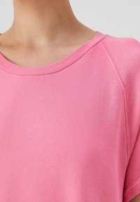 Sudadera rosa con un escote amplio, mangas cortas y una tela texturizada. Presenta un cuello de canalé y detalles de costura ligera.