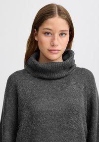 Maglione grigio a maglia con un alto collo a rovescio. Il tessuto è testurizzato, morbido e leggermente peloso, caratterizzato da una vestibilità ampia.
