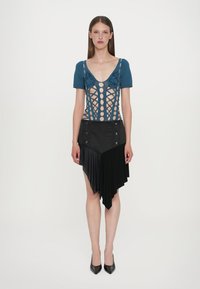 Haut en tricot bleu avec un design en treillis et de grands découpes circulaires ; jupe asymétrique noire avec des plis et des détails de boutons. Chaussures à talons hauts.