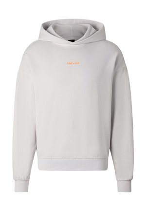 Jong persoon met kort blond haar, een witte hoodie, lichtgrijze cargoshorts, witte sokken en grijze sneakers, staand tegen een effen achtergrond.