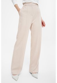 Beige weite Hose aus glattem, strukturiertem Stoff mit Fronttaschen und dezenten Steppnähten entlang der Nähte.