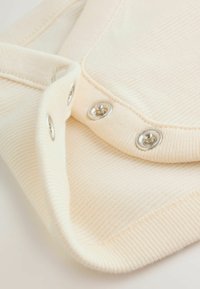 Krämfärgad ribbad tyg med metalliska tryckknappar, slät textur och en vikt kantdetalj som framhäver enkel, funktionell design.