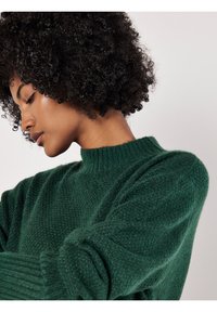 Grüner, strukturierter Pullover mit hohem, geripptem Halsausschnitt und langen Ärmeln. Weiches Material mit einem leicht lockeren Schnitt, das eine satte Farbe zeigt.