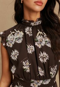 Sötétbarna ruha virágmintákkal, fehér és világoslila színekben, magas, fodros nyakkivágással és a derekán ráncolt anyagrésszel.