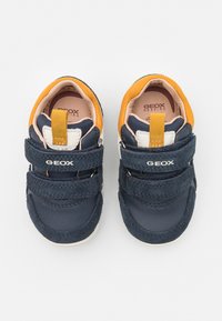 Scarpe da bambino blu navy in pelle e suede, con due cinturini in velcro, una morbida zona caviglia arancione e suole bianche.