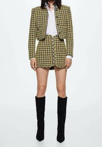 Keltainen ja musta houndstooth-blazer, jossa on yhteensopiva hame, teksturoitu kangas, lyhennetty malli, yhdistetty mustiin polven ylle ulottuviin saappaisiin.