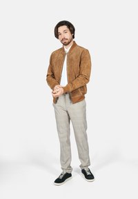 Chaqueta bomber de ante marrón con puños y cuello de canalé, combinada con pantalones de cuadros grises y zapatillas oscuras, creando un look informal.
